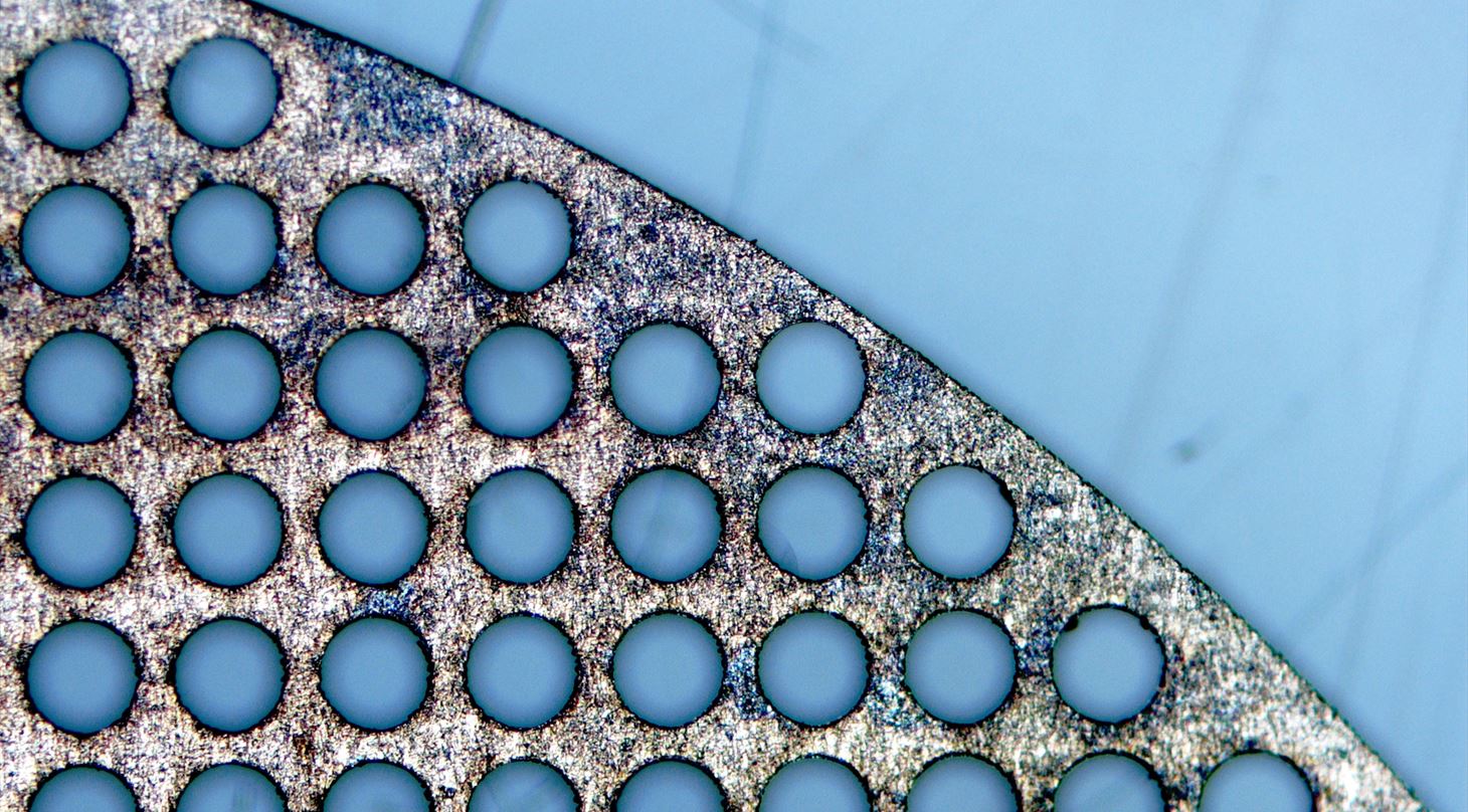 Billede fra optisk mikroskop der viser en metalprøve der er gennemboret med huller via laserbearbejdning